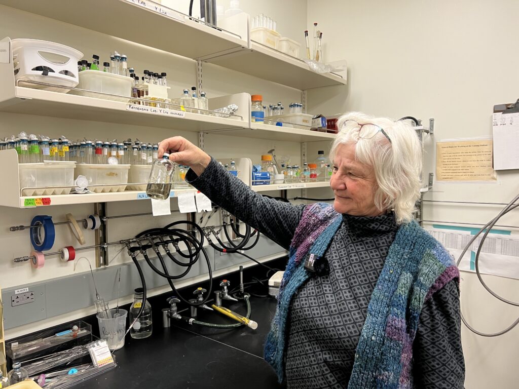 A researcher holds up a small bottle in a culture lab.