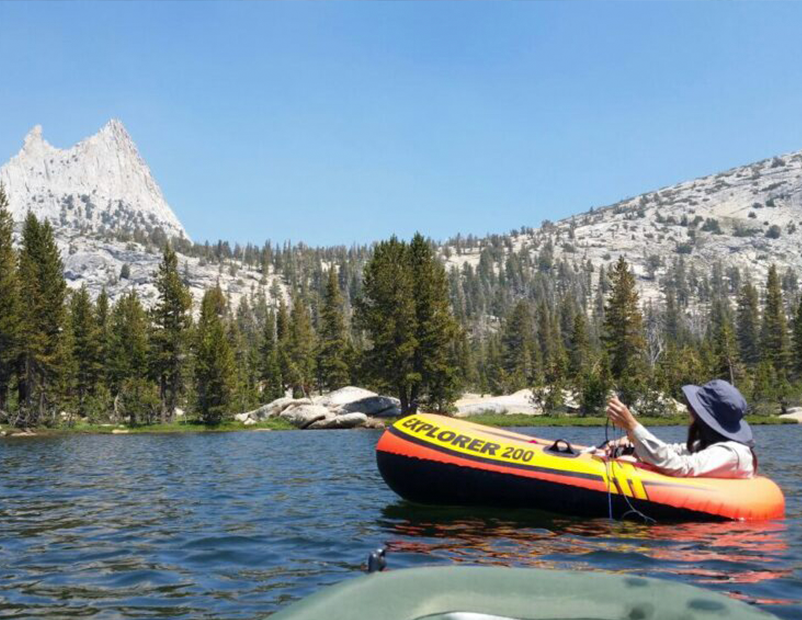 A scientist in a small orange raft paddles out in a freshwater lake.